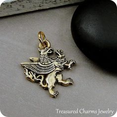 This Griffin Charm comes with a gold jump-ring as pictured. Please note that photo is not to scale and may appear larger to show detail. Refer to exact measurements below.Additional attachments (lobster clasp, large-hole bead, necklace chains) are available from the charm-attachments drop-down menu.  For a visual example of the different attachments and what each one is best suited for, scroll through the photos until you see the example photo or visit https://etsy.me/2BY7DAW for detailed inform Gold Fantasy Pendant Jewelry, Griffin Meaning, Medieval Griffin, Griffin Necklace, Bronze Vintage Amulet Charm Jewelry, Yellow Gold-plated Charms With Lobster Clasp, Pandora Beads, Large Hole Beads, Necklace Charm