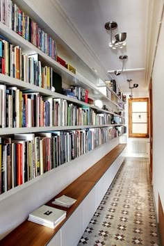 a long bookshelf filled with lots of books next to a wall full of books