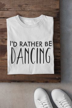 "Experience comfort and style in one with our \"I'd Rather Be Dancing\" text t-shirt. This unisex graphic tee is the perfect blend of fashion and passion, making it a great gift for dance lovers or a unique addition to your own casual wear collection. Crafted from high-quality, breathable cotton, this t-shirt ensures a comfortable fit for everyday wear. Its unique typography design features the expressive quote \"I'd Rather Be Dancing,\" making it an ideal choice for anyone who loves to express their love for dance. Whether you're heading to a dance class, running errands, or lounging at home, this tee lets you celebrate your passion in style. The neutral design suits various outfits and occasions. Don't miss out on this fun and fashionable dance quote shirt. It's not just a shirt; it's a Dance Shirts Ideas, Dance Quote, Unique Typography, Dance Shirt, Text T Shirt, Dance Lover, Dance Shirts, Quote Shirt, Dance Quotes