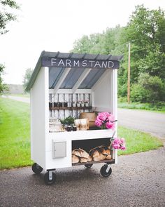 a small food cart with fresh produce on wheels and flowers in the front, outside