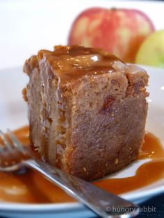 a piece of cake on a plate with caramel sauce and apples in the background