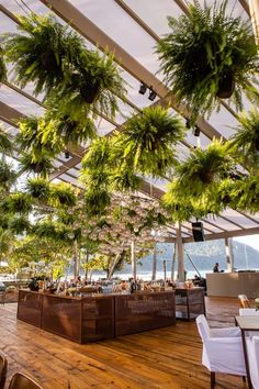 an outdoor bar with palm trees hanging from it's ceiling and chairs around it