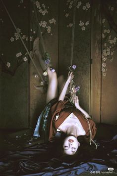 a woman laying on top of a bed next to a wooden wall with flowers hanging from it