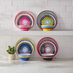 three colorful plates sitting on top of a white shelf next to a potted plant