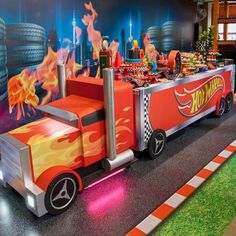 a toy truck with flames on the side driving down a track in front of a wall