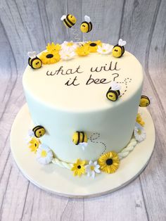 a white cake with yellow flowers and bees on it that says what will it bee?