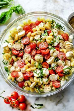 a glass bowl filled with pasta salad next to tomatoes and parsley on the side