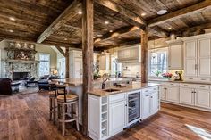 an open kitchen and living room area with wood beams on the ceiling, white cabinetry, and hardwood flooring