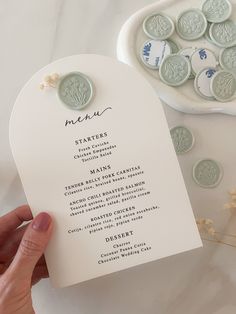 a person holding up a white menu card with buttons on it next to some flowers