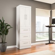 a tall white cabinet next to a plant in a living room with hardwood flooring