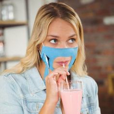 a woman with a mask on her face holding a pink smoothie in front of her face