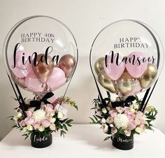 two vases filled with balloons and flowers on top of a white table next to each other