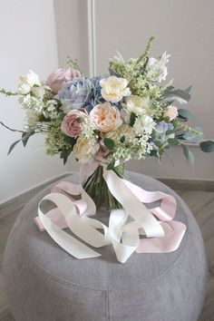 a bouquet of flowers sitting on top of a round ottoman with ribbon around the bottom