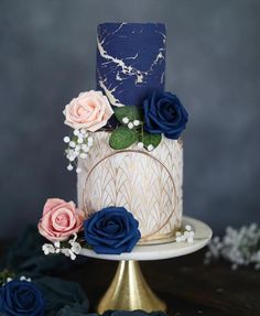 a three tiered cake with blue and pink flowers on top is sitting on a gold pedestal