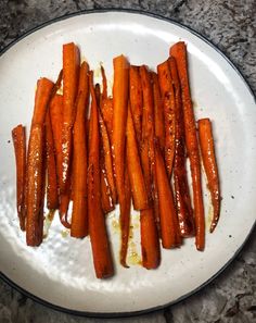 cooked carrots on a white plate sitting on a granite counter top with oil drizzled over them