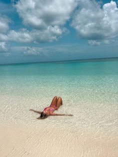 a woman laying on her back in the water at an empty beach with blue skies and white clouds