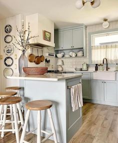 a kitchen with wooden stools and white counter tops in front of an island that has plates on it