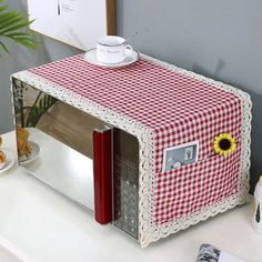 a red and white checkered table cloth covering a microwave oven with a coffee cup on top