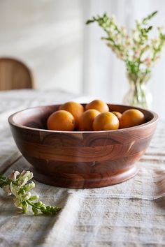 a wooden bowl filled with oranges sitting on top of a table next to a vase