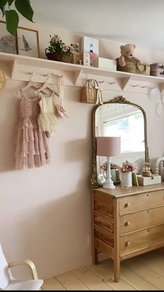 a room with a dresser, mirror and teddy bear on the wall above it is a shelf that holds baby's clothes