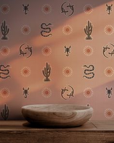 a bowl sitting on top of a wooden table in front of a wall with cactus designs