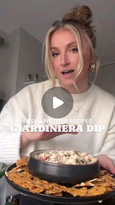 a woman holding a platter with food on it and talking to someone in the background