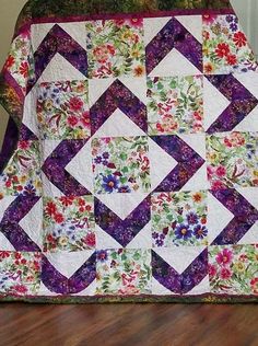 a purple and white quilt sitting on top of a wooden floor