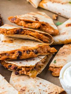 several quesadillas are stacked on top of each other with sour cream in the background