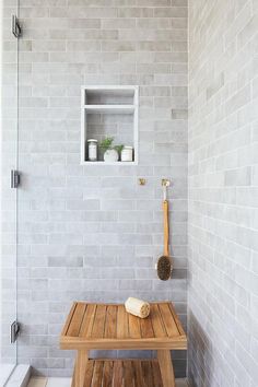 a wooden bench sitting in front of a white brick wall next to a walk in shower