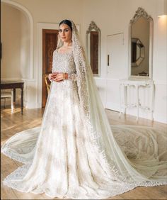 a woman in a white wedding dress standing on a wooden floor with a long veil over her head