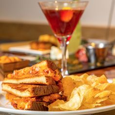 a white plate topped with lots of food next to a glass filled with liquid and chips