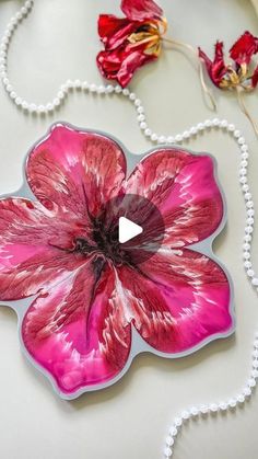 a pink flower on a white table with beads and flowers in the back ground,