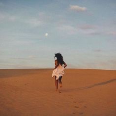 a woman is running across the desert in a white dress and headdress on