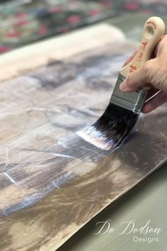 a person is holding a paintbrush and painting on a piece of metal