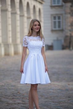 a woman in a white dress standing on a cobblestone street with an old building in the background