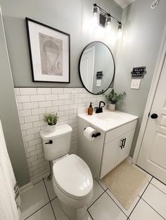 a white toilet sitting next to a sink in a bathroom under a round mirror on the wall