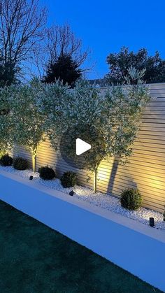 an outdoor garden with trees and bushes lit up at night in the background is a white fence