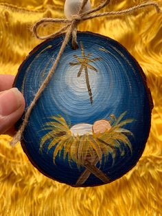 a hand holding a painted ornament with palm trees and a baby jesus in the manger