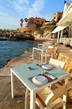 an outdoor dining area overlooking the ocean with tables and chairs set up for two people