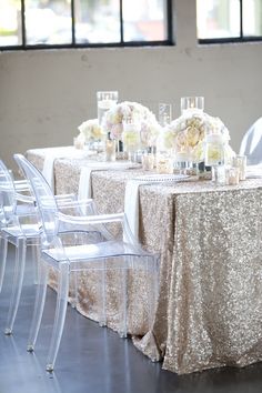 the table is set with clear chairs and white flowers