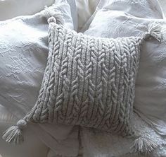 a close up of a pillow on a bed with white linens and tassels