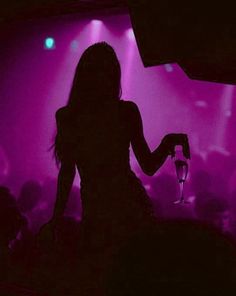 the silhouette of a woman holding a wine glass in front of a purple lit room