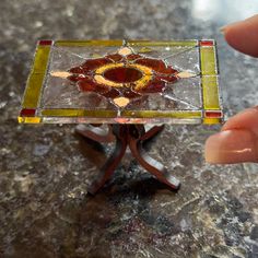 a hand holding a small stained glass object on top of a marble table with a metal stand