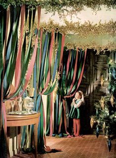 a child standing in front of a christmas tree with ribbons hanging from it's ceiling