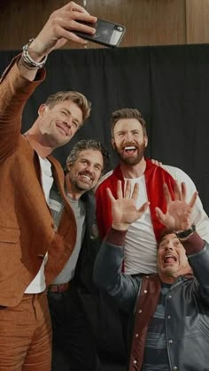 three men are taking a selfie with their cell phone while standing in front of a black backdrop