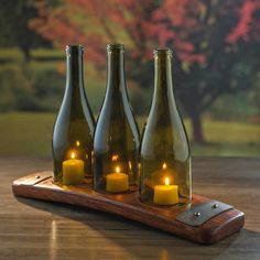 three wine bottles with candles in them on a wooden tray