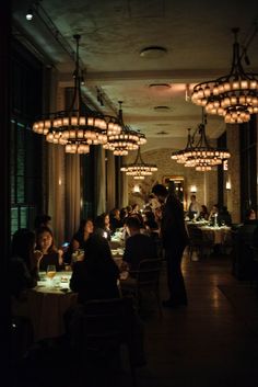 people are sitting at tables in a dimly lit dining room with chandeliers hanging from the ceiling