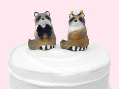 two raccoon figurines sitting on top of a white cake