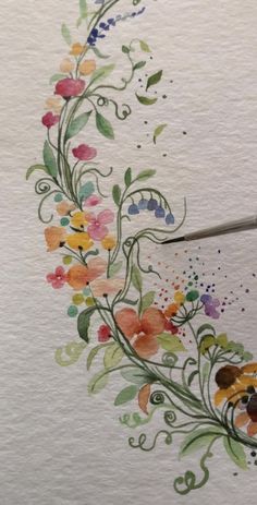 a watercolor painting of flowers and leaves with a blue brush on top of the paper