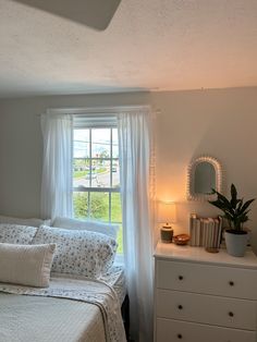 a bedroom with a bed, dresser and window that has white curtains on the windowsill